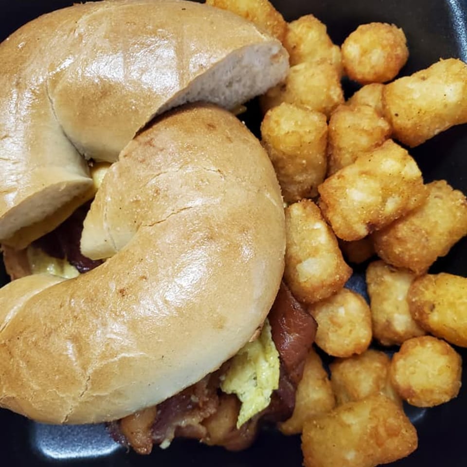A bagel sandwich with bacon and egg, served with a side of golden tater tots.