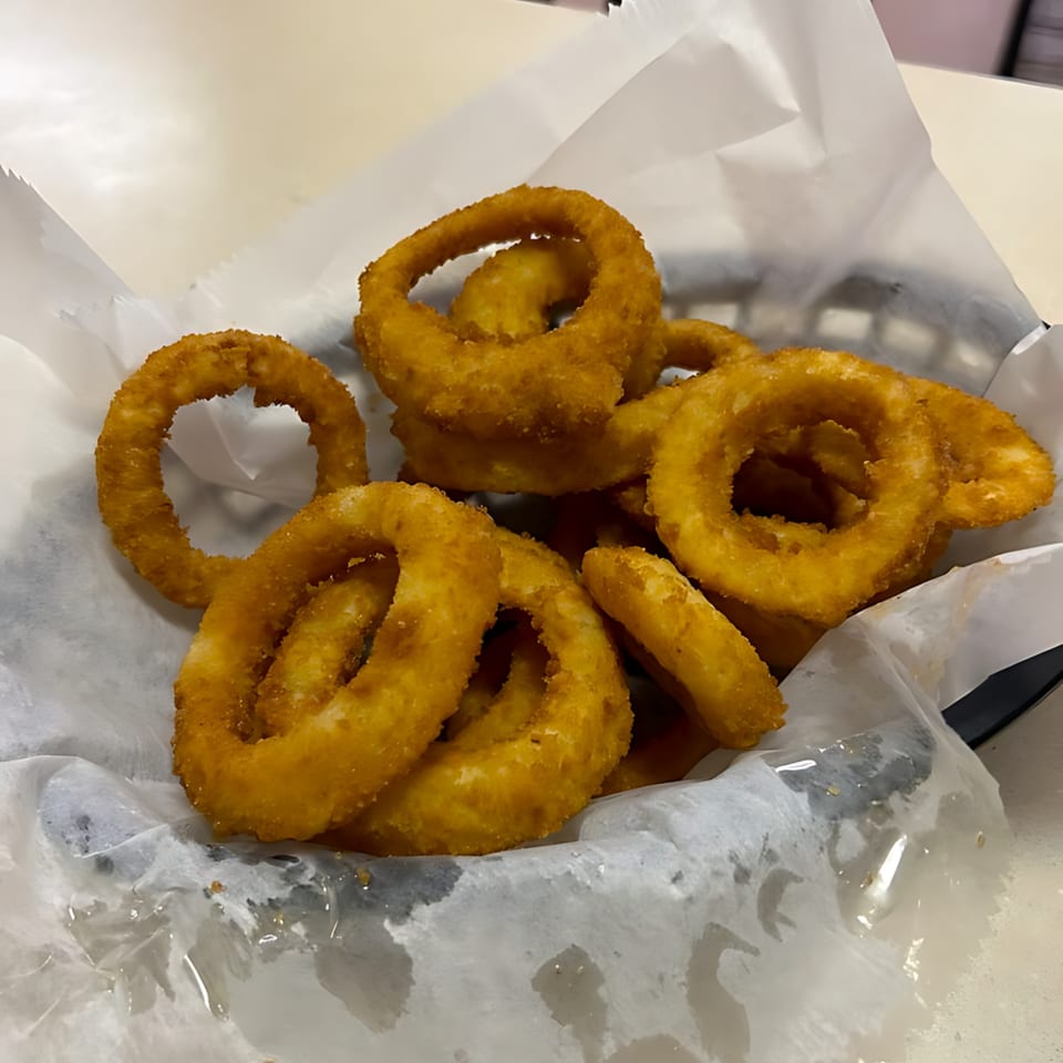Golden-brown, crispy onion rings served in a black basket lined with white paper at Romano's Deli Pizzeria.