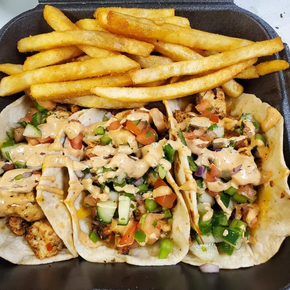 Three chicken tacos with pico de gallo and sauce, served with a side of french fries.