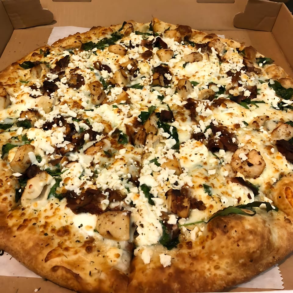 A Romano's Deli Pizzeria pizza with chicken, spinach, and feta cheese in a box.