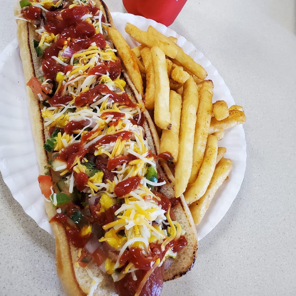 A loaded hot dog with cheese, relish, and ketchup, served with a side of golden french fries.