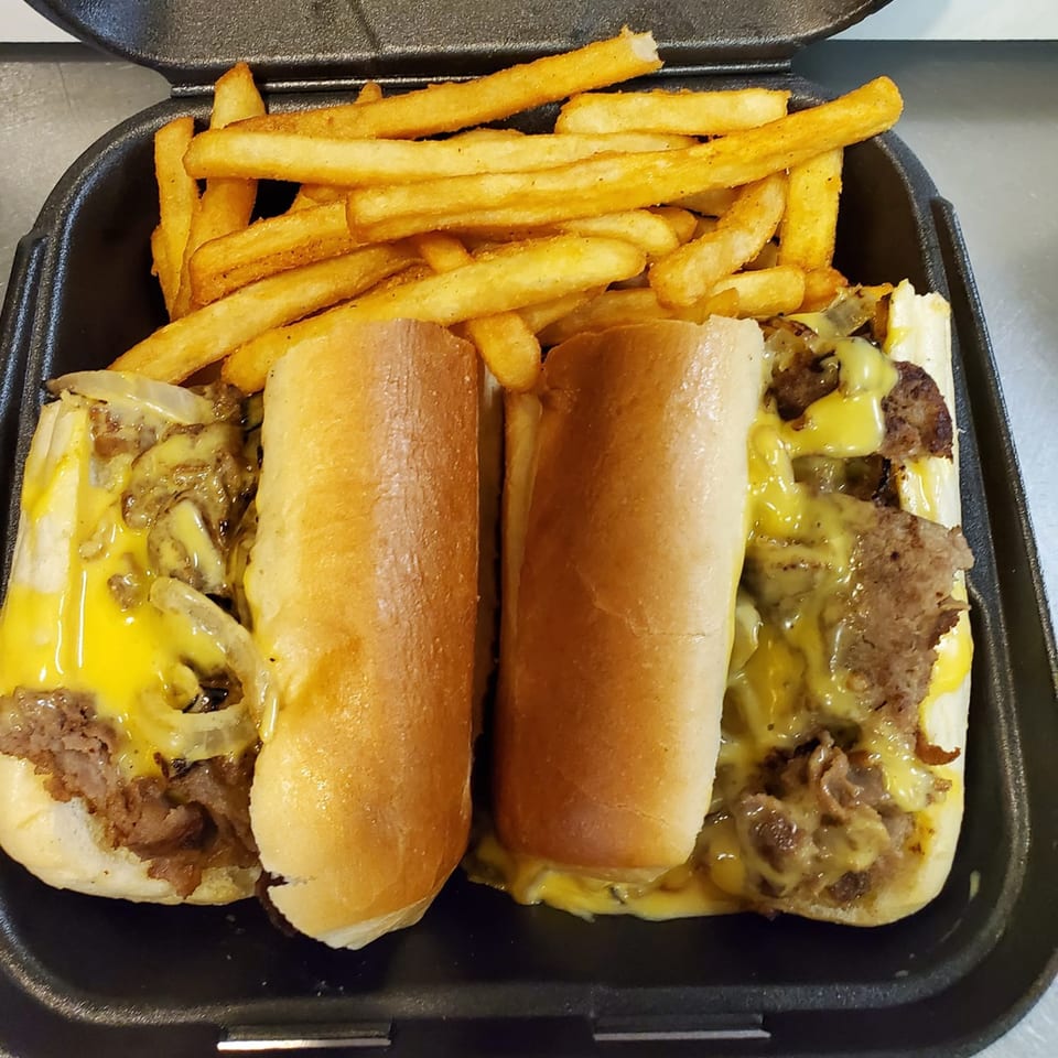 Two cheesesteak sandwiches with melted cheese and onions, served with a side of golden fries.