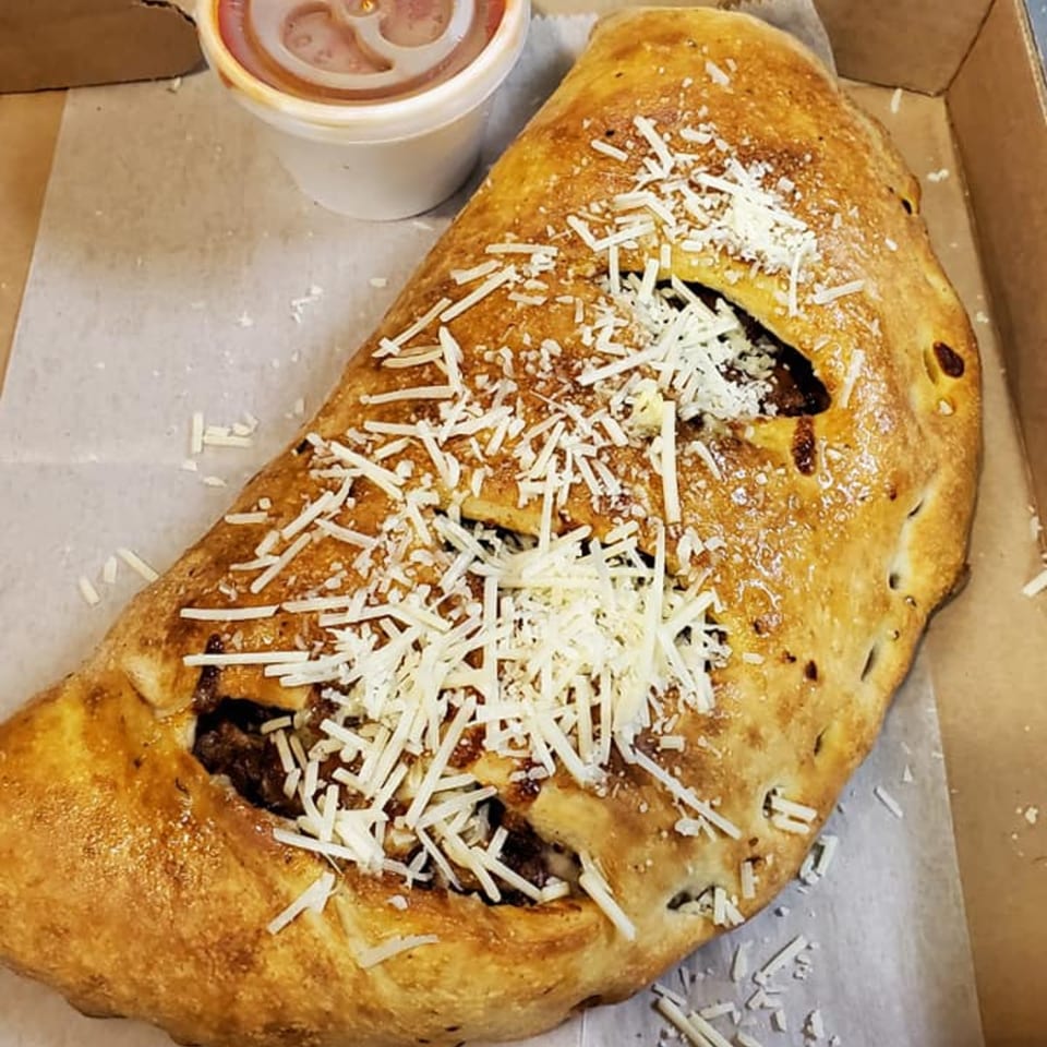 A Romano's Deli Pizzeria calzone, topped with shredded cheese, and a side of marinara sauce.