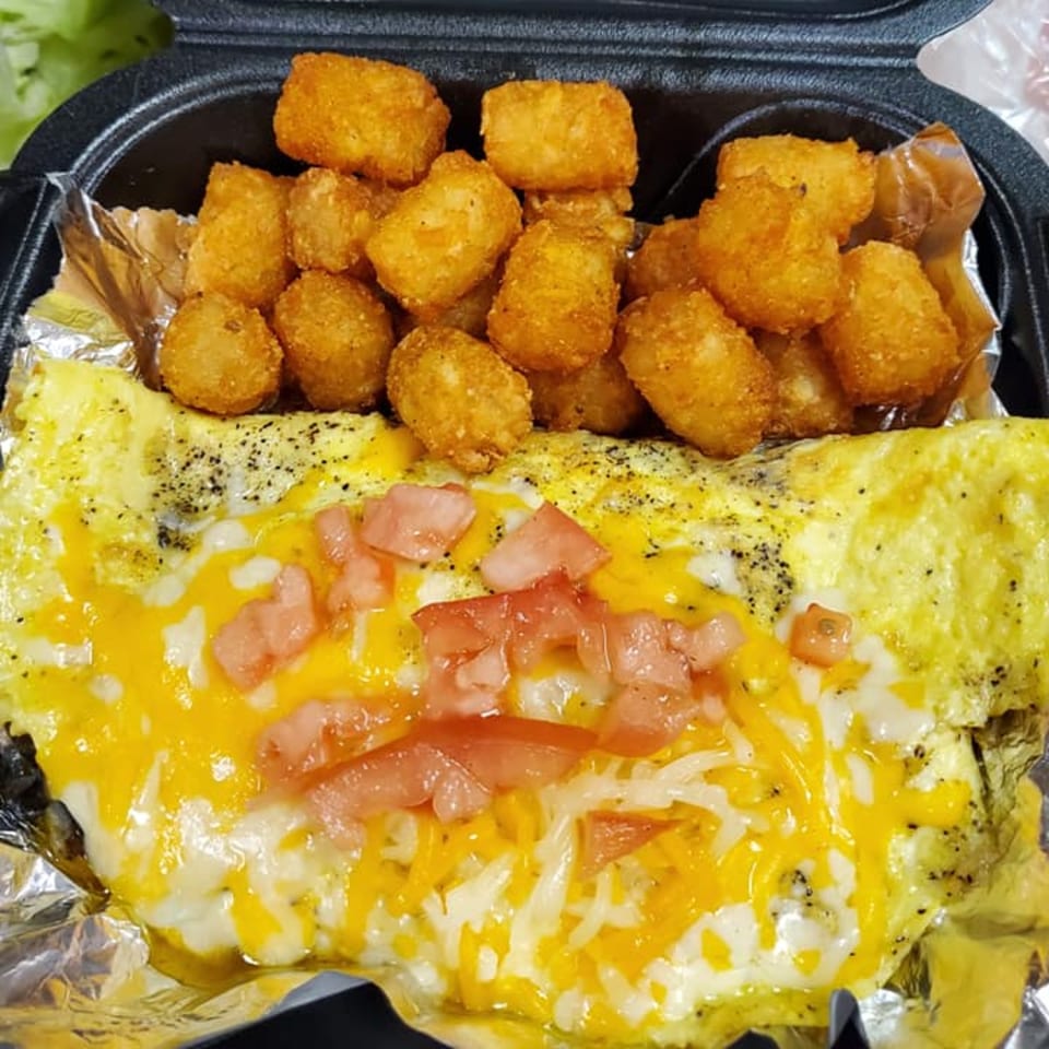 Cheesy omelet topped with diced tomatoes and a side of crispy tater tots in a black container.