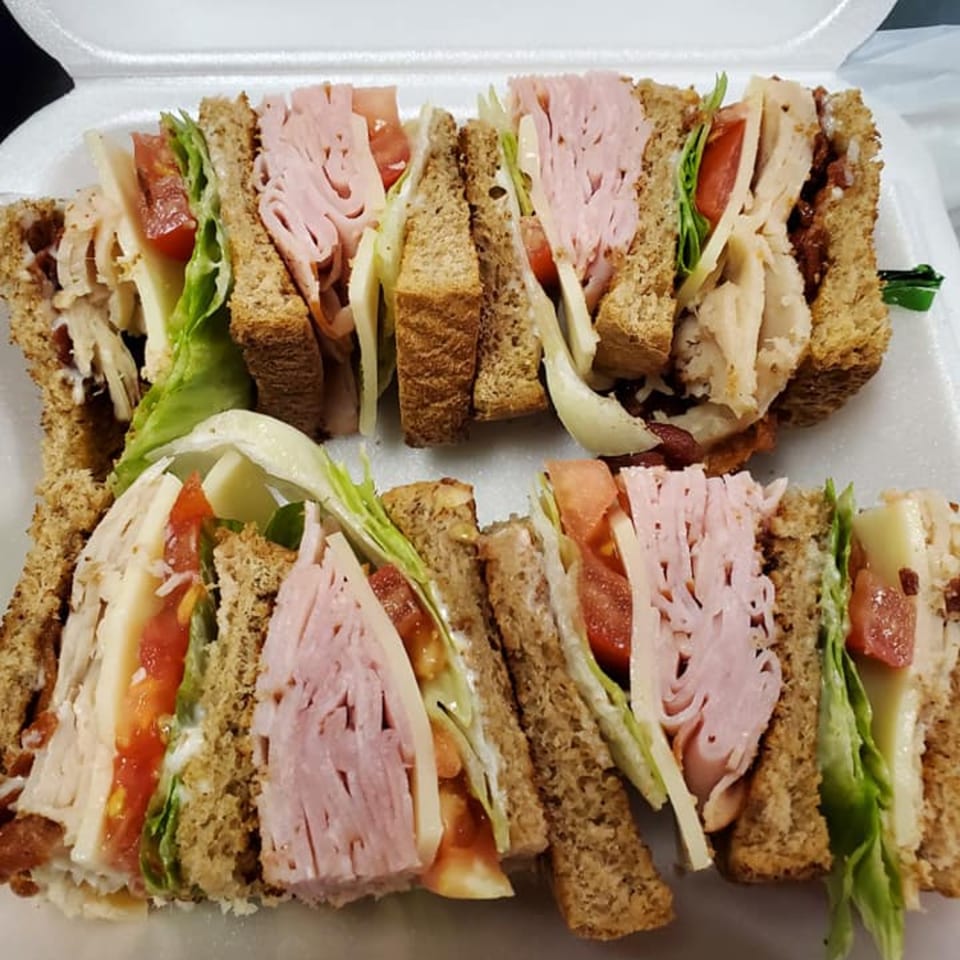 Two large deli sandwiches, cut into quarters, filled with meat, cheese, lettuce, and tomato.
