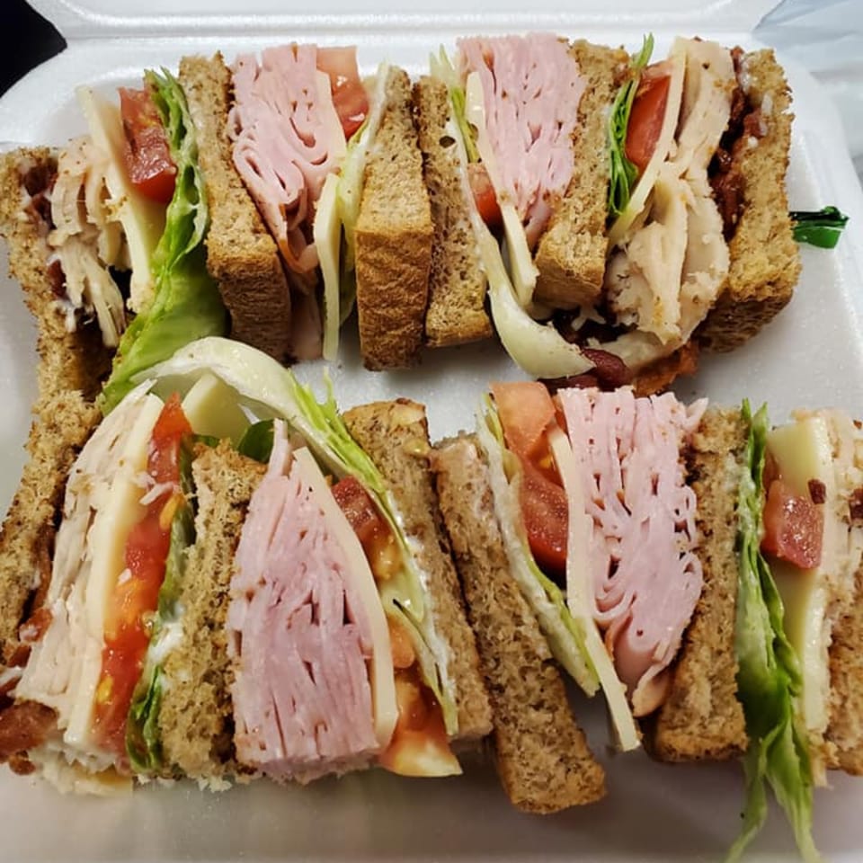 Two club sandwiches with ham, turkey, bacon, lettuce, tomato, and cheese on wheat bread.